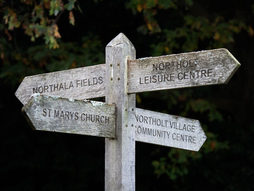 A weathered wooden signpost with four directional arms, each showing signs of age and exposure with peeling paint and rough, greyish-brown surfaces. The top arm points to the right and reads 'Northolt